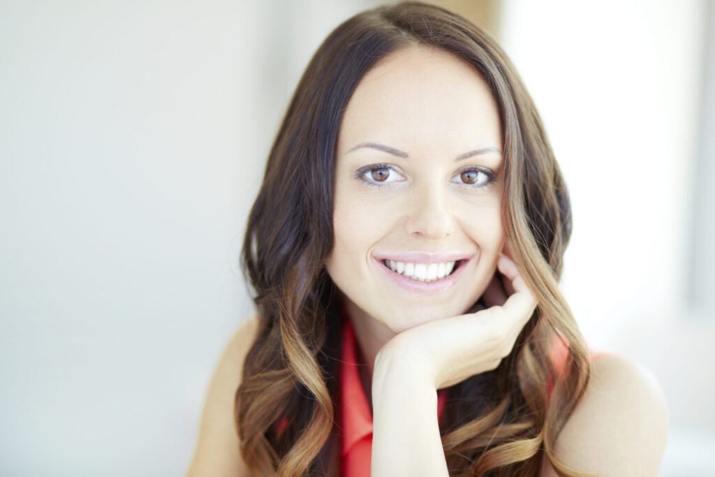 female with brown hair in red shirt with hand under chin