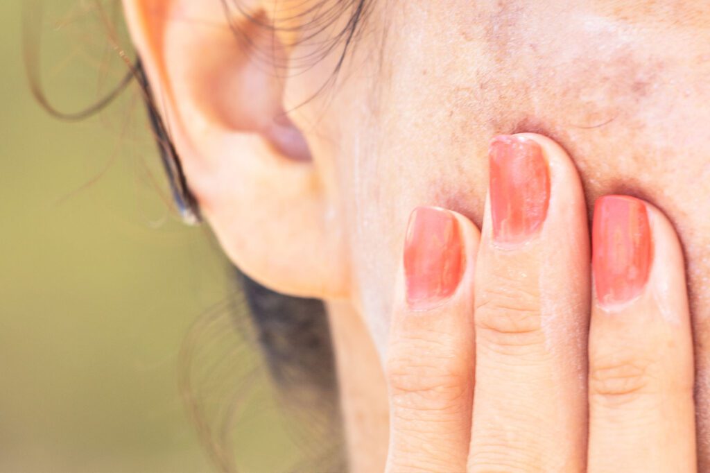 female with red nail polish touching face