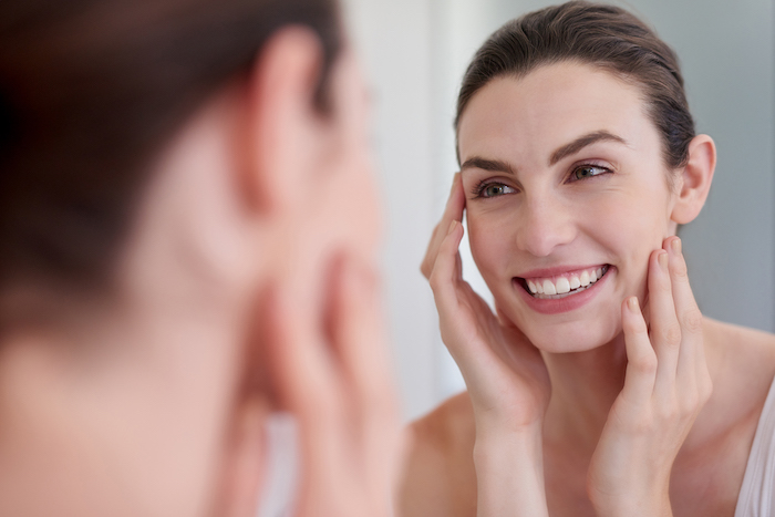 brown hair female looking in mirror and touching face