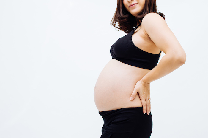 brown hair pregnant female showing her belly in black pantss and sports bra
