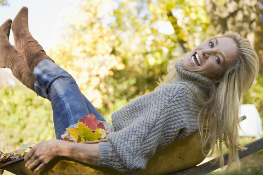 blonde female with gray sweater in wheelbarrow in the fall