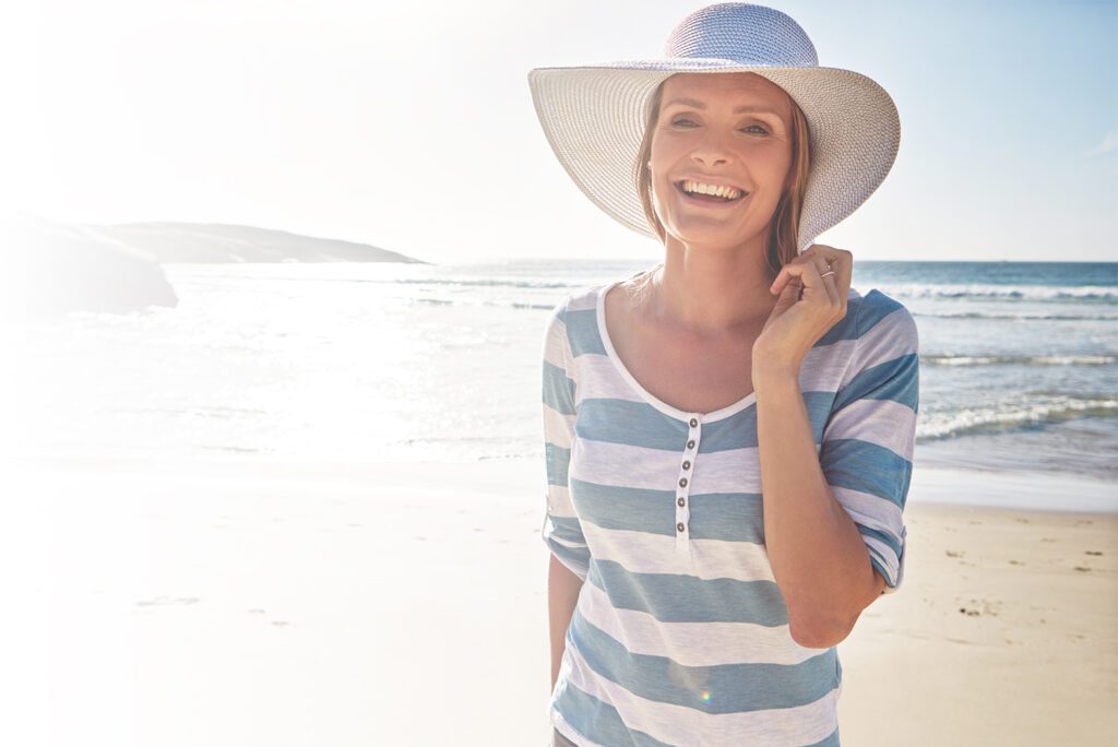blonde female on beach in striped shirt with white sun hat