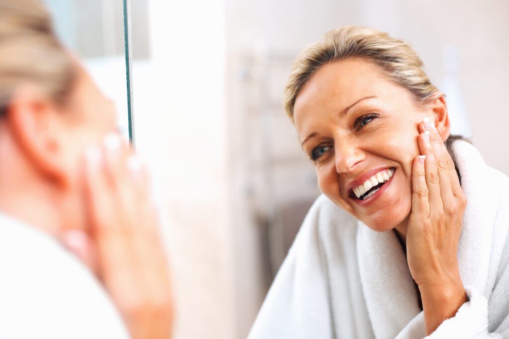 blonde female looking in mirror touching her face