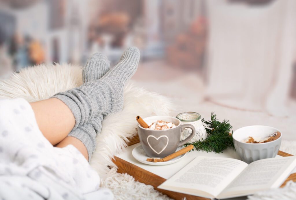 female in warm gray socks sitting next to hot chocolate and an open book