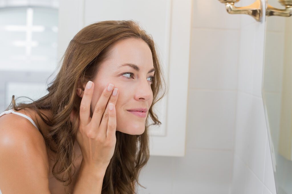 brown hair female looking in mirror touching her face